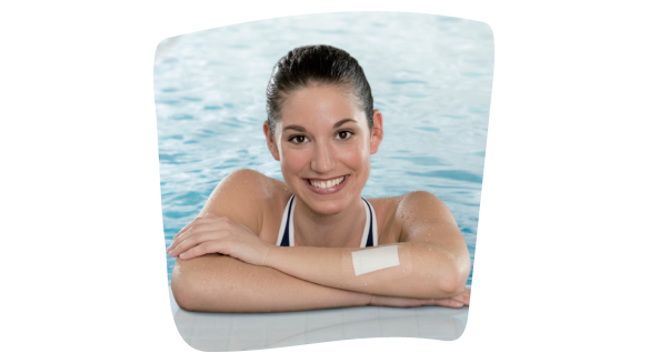 Imagen de una chica joven apoyada en el bordillo de una piscina, sonriendo, con los brazos cruzados y un apósito impermeable para cubrir una herida en el antebrazo izquierdo. Imagen de una chica joven apoyada en el bordillo de una piscina, sonriendo, con los brazos cruzados y un apósito impermeable para cubrir una herida en el antebrazo izquierdo.